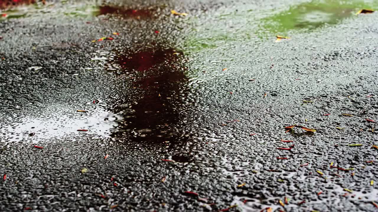 Rain drops falling on asphalt with reflections