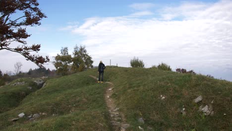 blonde woman in sport clothes walking on top of hill in autumn, blue sky and trees on scene