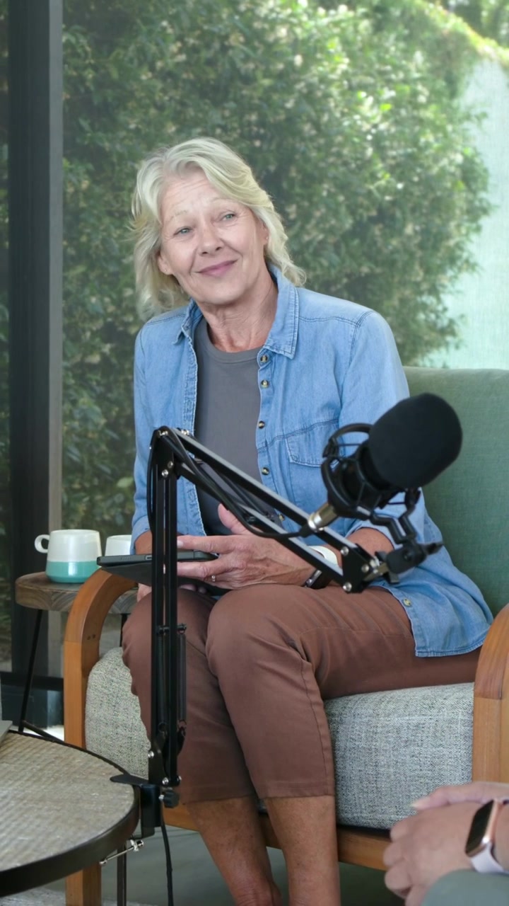 Vertical video: Smiling denim host reacting to offframe voice replying for podcast with mic tablet