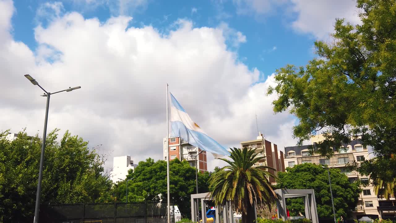 Bandeira da Argentina tremulando ao vento sobre um parque urbano verde e o horizonte da cidade.