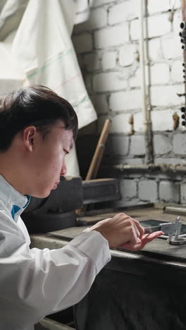 vista posterior de una persona que observa como un joven técnico en bata blanca de laboratorio trabaja en una tableta y recoge equipos de precisión en un taller automotriz con herramientas y maquinaria en el fondo
