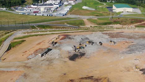 Aerial-view-of-landfill,-trucks-and-equipment-at-dump,-manufacturing-plant-in-background,-Pennsylvania-USA