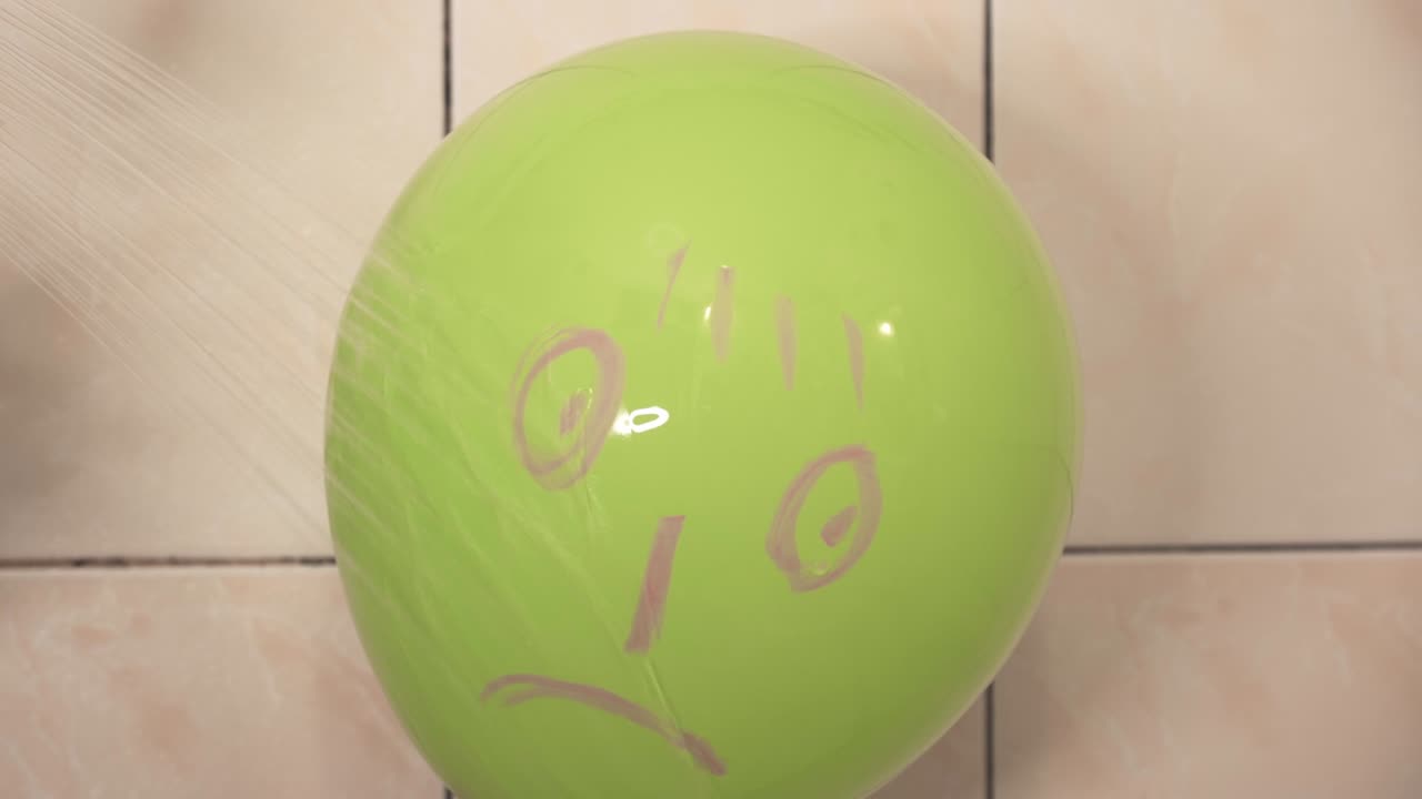 un rostro descontento pintado en un globo toma una ducha. chorros de agua se derraman en la cara.