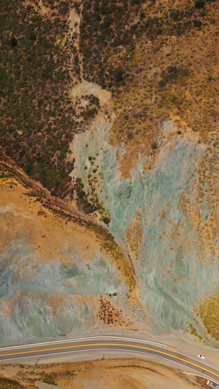 Weird dry landscape covered with moss and lichens. Motorway passing through the bare rocks of California coastline. Aerial view. Vertical video