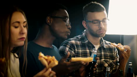 multiethnic group of young people enjoying pizza and drinks at a casual house party. friends eat fast food and dance