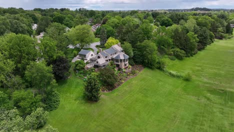 luxury shingle style mansion in upper class housing area of america. aerial approaching shot. well-kept and neat garden with flowers and plants in spring. sunny day in suburb. located on hilltop.