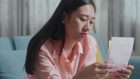 close up of asian woman with a laptop looking at the bill and being sad while sitting on sofa at home