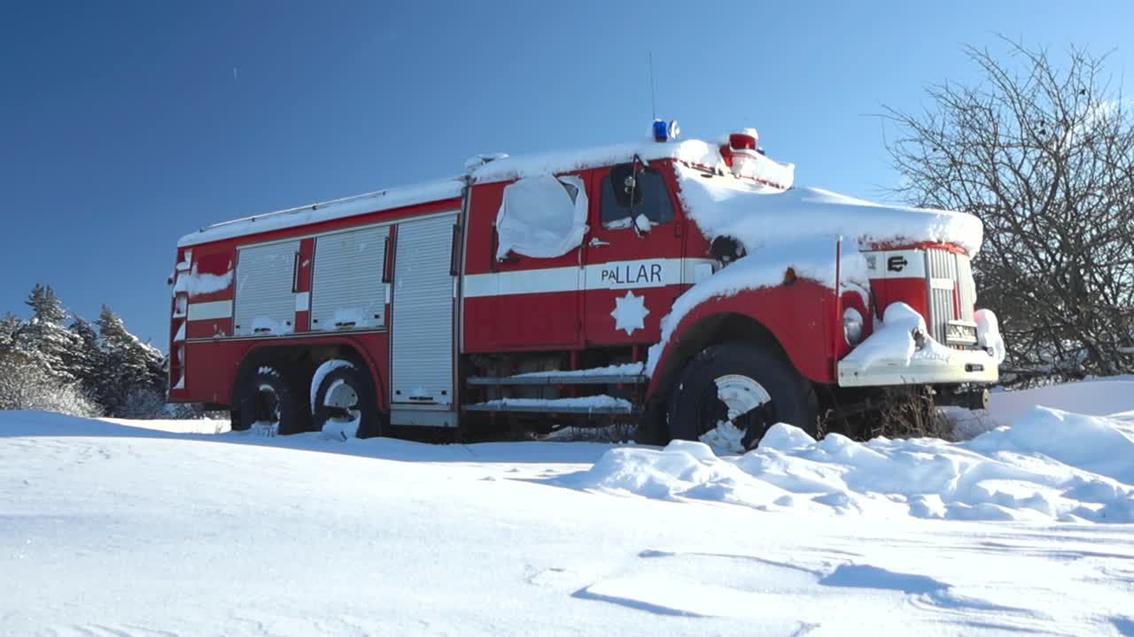 Old vintage and retro red and white firetruck abandoned in snow during a winter snowy and sunny day. Sky is blue in the background with white thick and fluffy snow in the foreground on the ground.