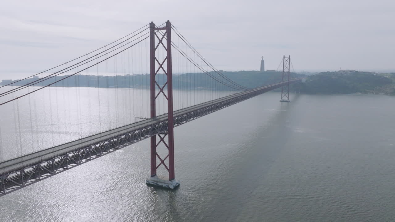 Cinematic aerial drone view of the empty red 25th April suspension bridge over the Tagus river in Lisbon, Portugal, with no cars or traffic before the running event