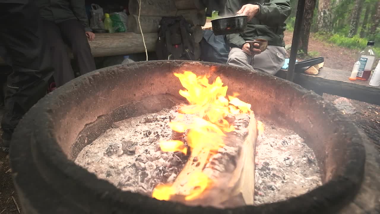 Group of friends hanging around on a camping trip - campfire being warmed up for cooking