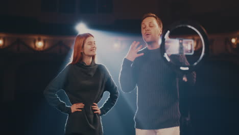 actor and actress showing stage smile for online audience adult man talking and young woman demonstrating stage smile while recording or streaming online tutorial video in spotlight on stage in theater