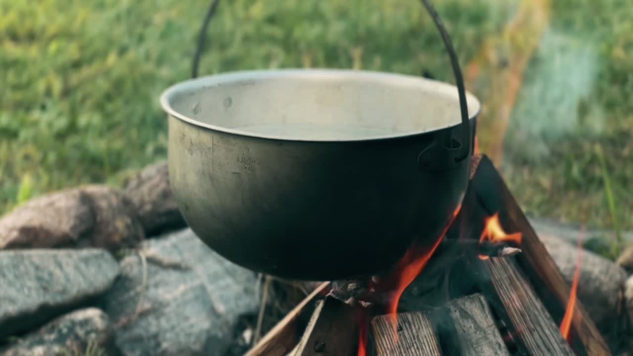 Sooty pot hanging over a crackling campfire, cooking a delicious meal outdoors on a warm summer day, enjoying the tranquility of nature while embracing the wilderness experience