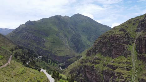 drone footage of a green mountain of the andes in peru. flying backwards. green trees and roads at the bottom and another mountain to the right.