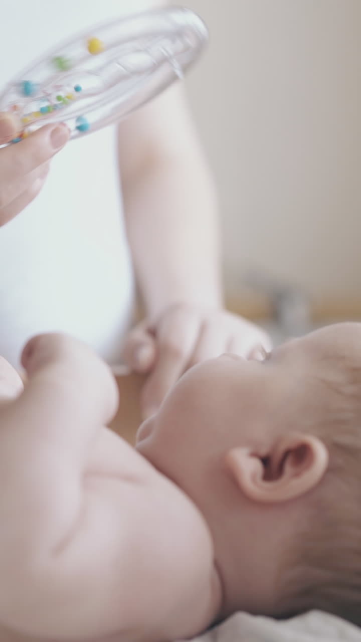 skilled nurse practices infant leg massage and mother distracts boy attention with round plastic toy close view
