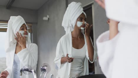 video of relaxed diverse female friends moisturizing faces in bathroom