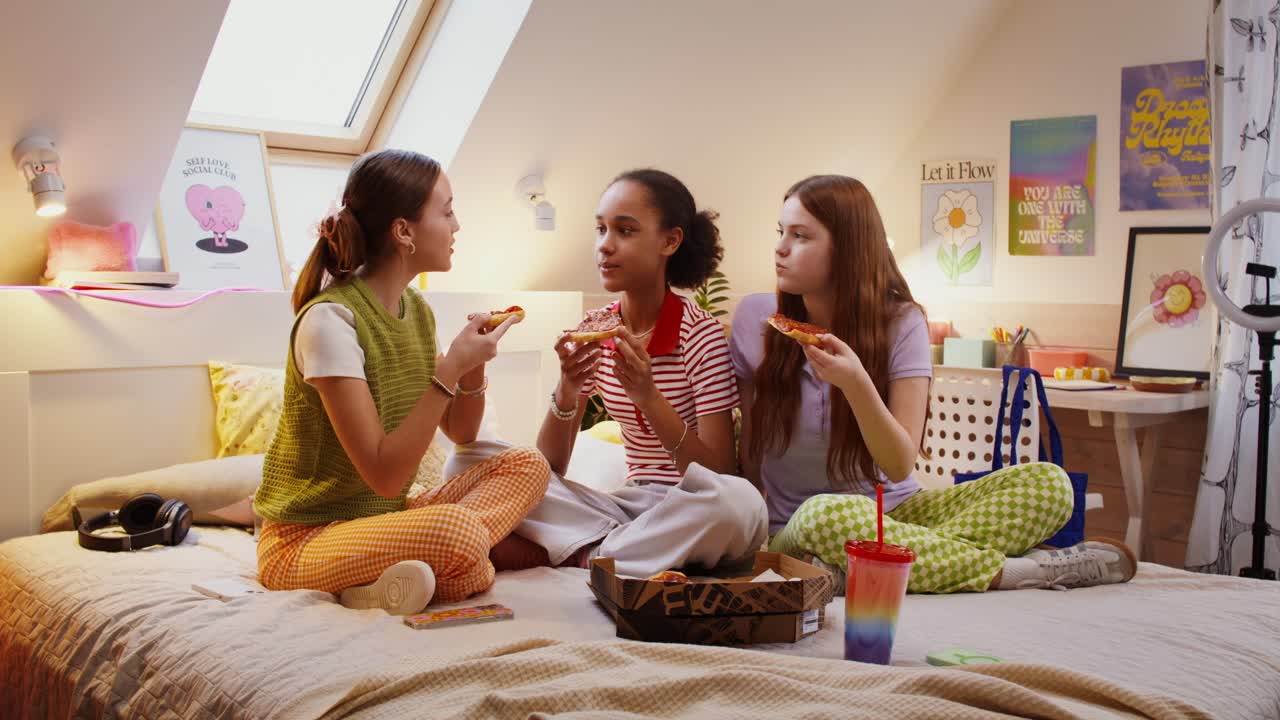 십대 친구들이 침실에서 피자를 즐기고 있습니다.