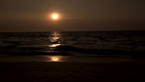 puesta de sol oscura con mar en primer plano y olas golpeando la playa