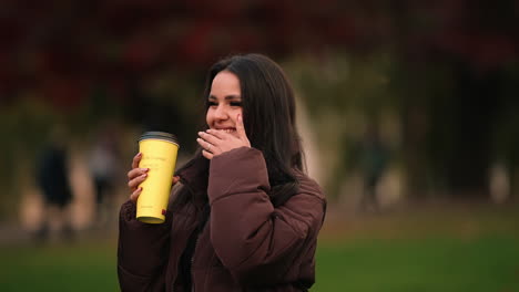 Una-Mujer-Encantadora-Sosteniendo-Un-Café-Riéndose-Del-Parque-De-Iulius,-Cluj-napoca-En-Rumania