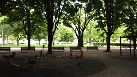 a view through milan italy public gardens showing few people around wearing face mask and kids playground unaccessible with police tape