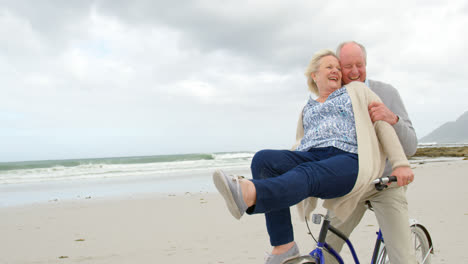 Front-view-of-old-caucasian-senior-couple-sitting-on-a-bicycle-at-beach-4k