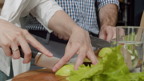 백인 부부가 현대 부엌에 있는 나무 도마에서 아보카도를 함께 자르는 모습을 클로즈업합니다.