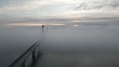 car drives over cable stayed bridge covered in dense fog