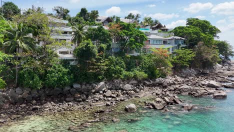 drone footage captures luxurious resorts along phuket's rocky coastline, showcasing lush greenery and turquoise waters under clear skies