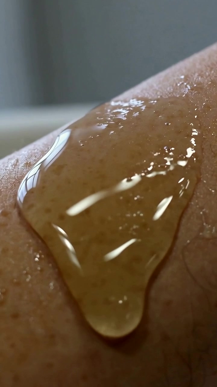 Video vertical: Pellizcando la yema del dedo para liberar gel ámbar sobre el brazo, formando una gota brillante para una prueba cutánea.