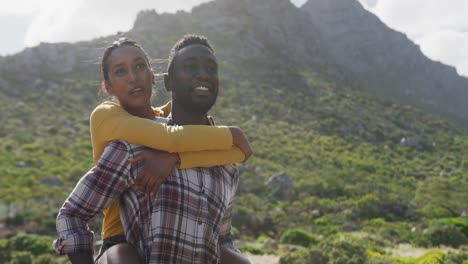 hombre afroamericano dando paseo a hombros a su esposa mientras hace senderismo en las montañas