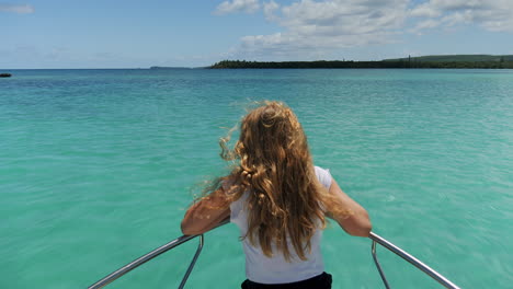 young girl with thick hair riding the bow motorboat as it speeds towards the isle of pines, new caledonia