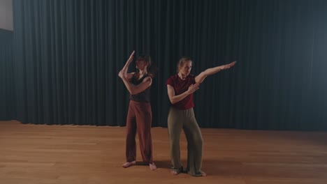 two dancers perform expressive choreography barefoot on wooden stage indoors