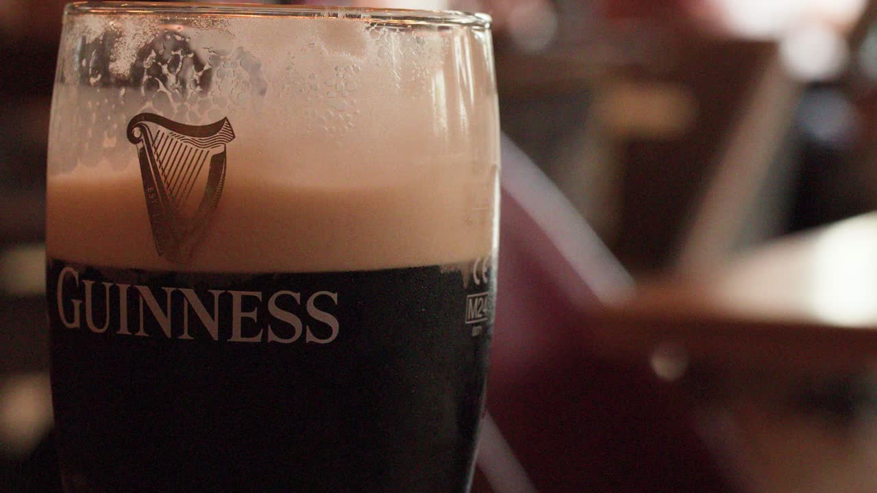 Dark stout beer settles in glass, creamy foam rising, pub background, shallow depth of field