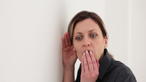 woman eavesdropping against a wall with a surprised expression