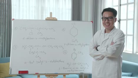 asian male teacher with glasses crossing arms and smiling to camera while teaching chemist at home