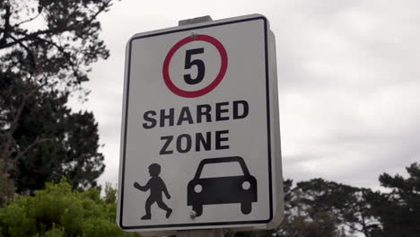 Five-kilometer-miles-speed-limit-shared-zone-sign-with-an-illustration-of-pedestrian-and-car-with-trees-in-the-background