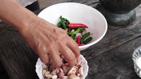 mano femenina poniendo ajo en un bol lleno de especias sobre una mesa de madera - preparación para cocinar