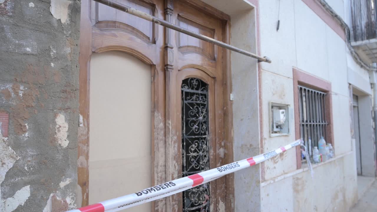 Facade of a building with a wooden door and firefighter caution tape after severe flooding in Chiva, Valencia. Effects of the DANA