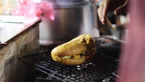 street vendor grilling sandwich on open flame