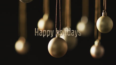 happy holidays text with silver christmas baubles hanging on dark background