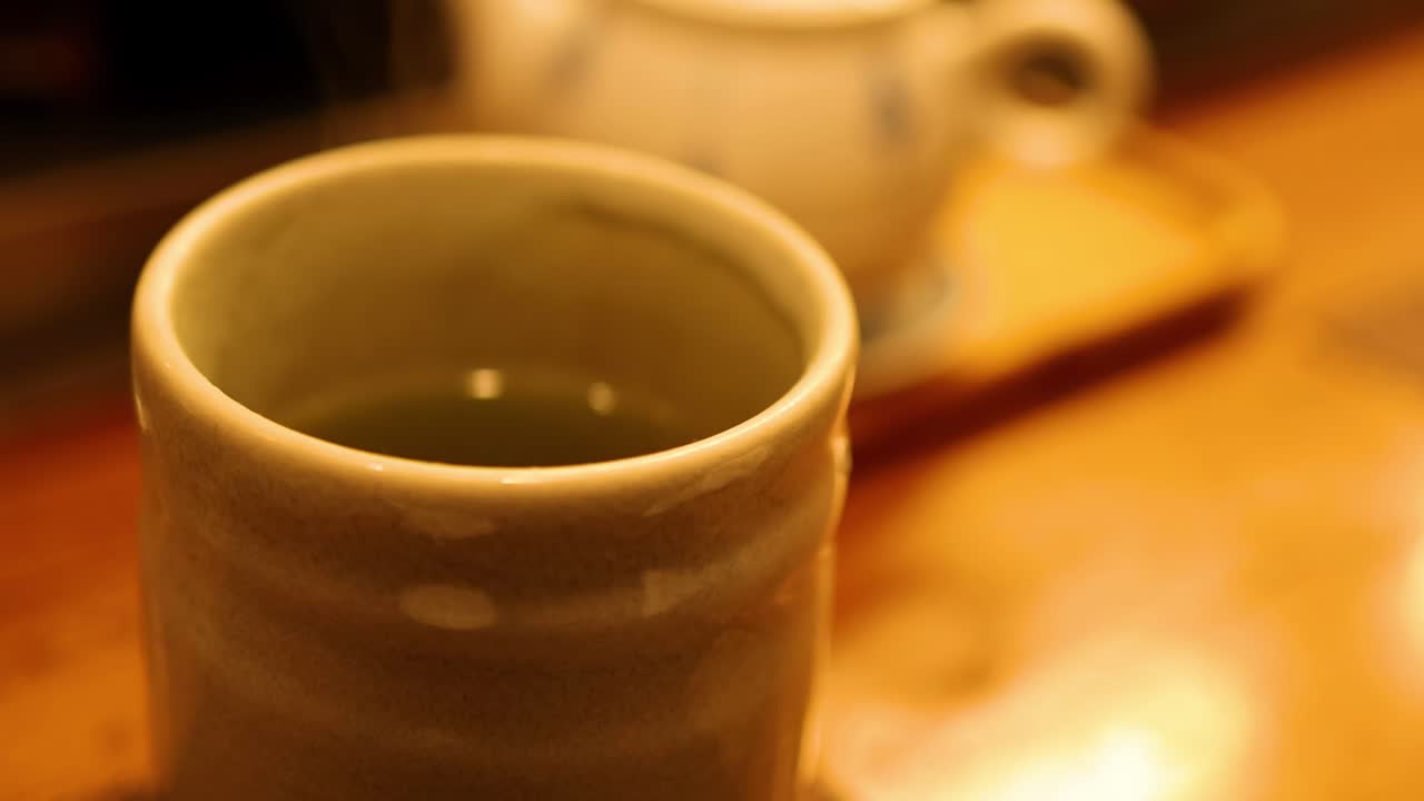 A ceramic cup sits on a warm, wooden surface with soft lighting in the background.