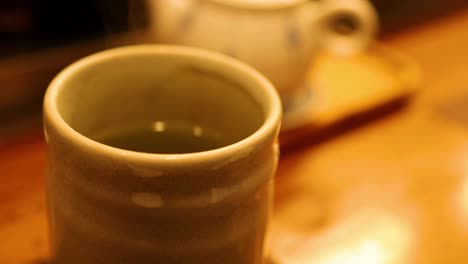 a ceramic cup sits on a warm, wooden surface with soft lighting in the background.