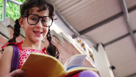 smiling schoolgirl reading book in campus at school