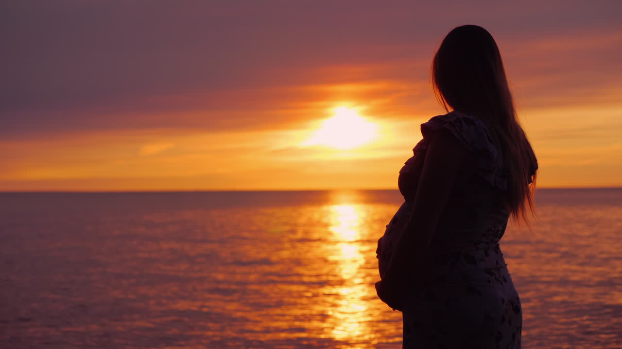 Silueta de una joven embarazada con el atardecer sobre el océano de fondo.