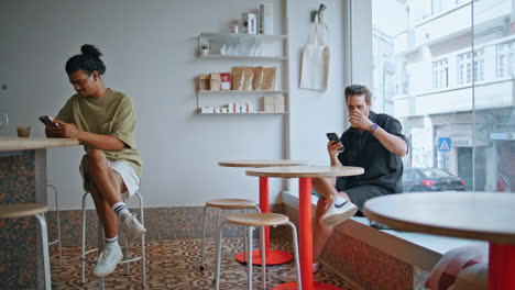 two guys sitting cafeteria looking at smartphone. cafe visitors relaxing coffee