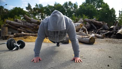 hombre motivado con chaqueta con capucha haciendo flexiones en el suelo al aire libre