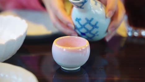 Japanese-Sake-Being-Poured-into-Cup-by-Women,-Close-up-Shot-4k