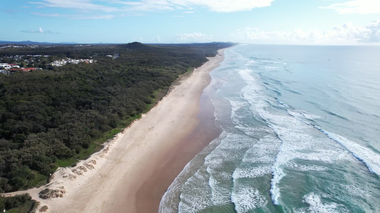 Bølger, der slår ind over den sandede kyst ved Coolum Beach med tæt skov i QLD, Australien – luftoptagelse
