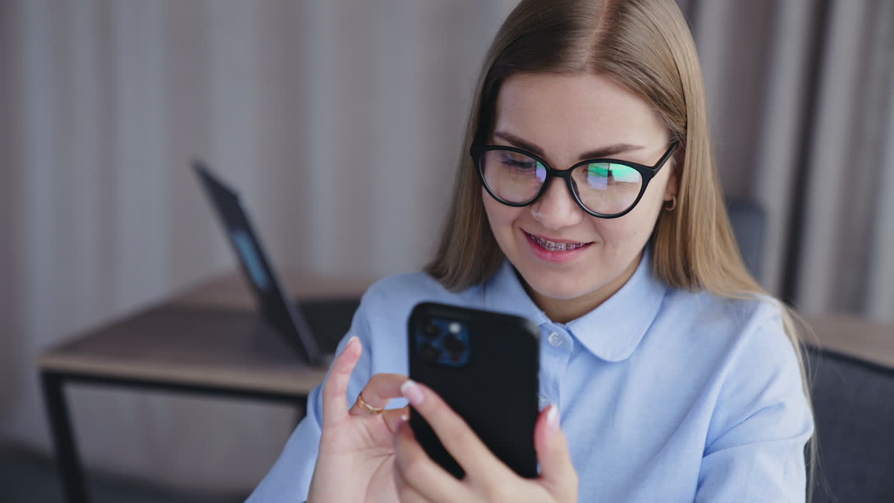 Beautiful young blonde woman in glasses holding phone in front of her face. Lady smiling and taking selfie on her smartphone. Close up.