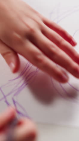 little girl draws fairy tale character portrait with purple color pencil on white paper sheet at art lesson in classroom extreme closeup slow motion