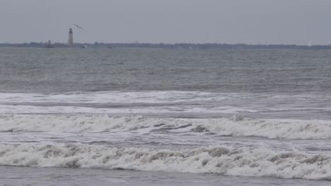 crashing waves on a winter day with defocused lighthouse in the distance, static medium shot